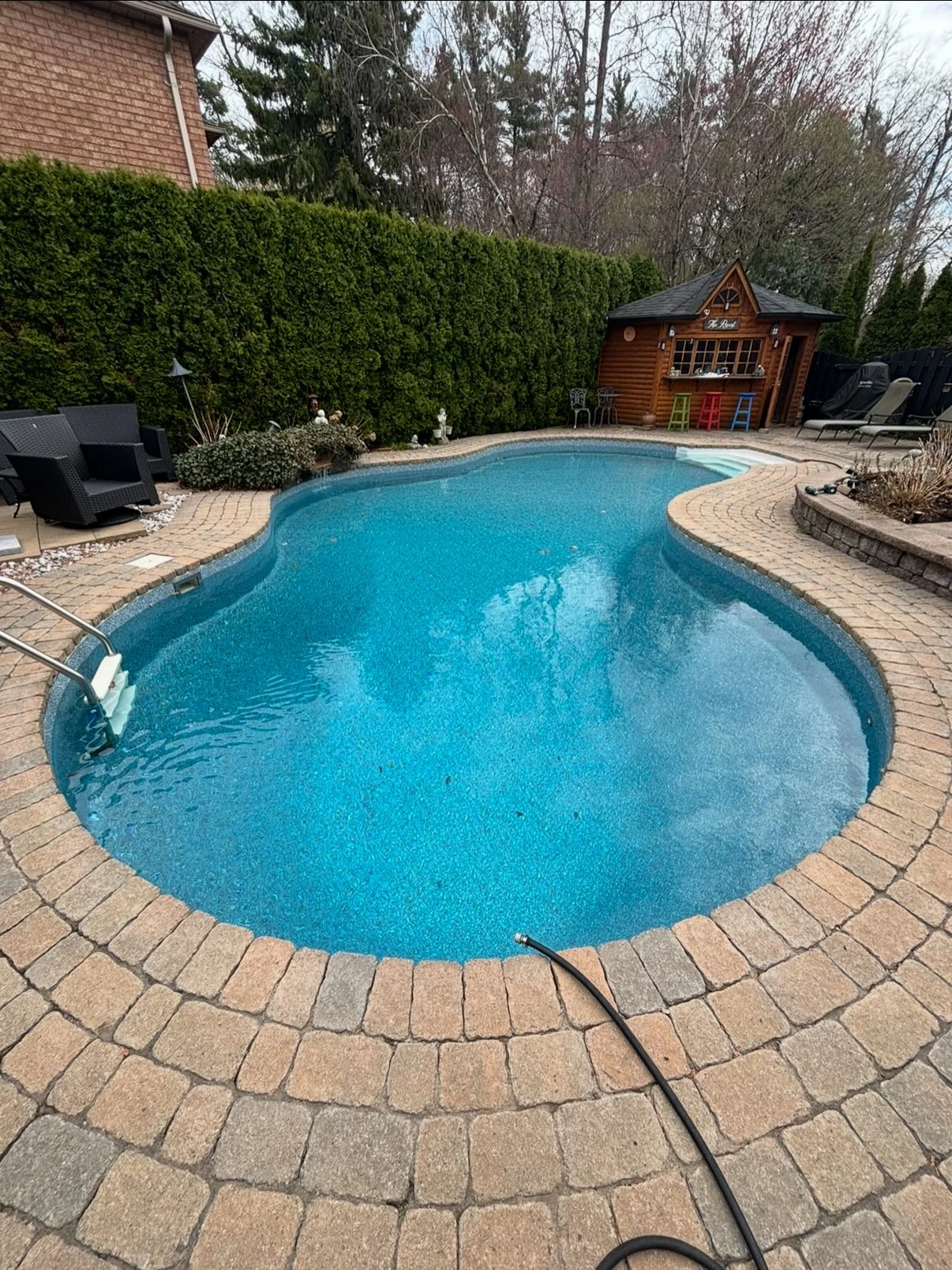 Kidney-shaped pool filled with blue water after new liner installation, surrounded by a brick patio