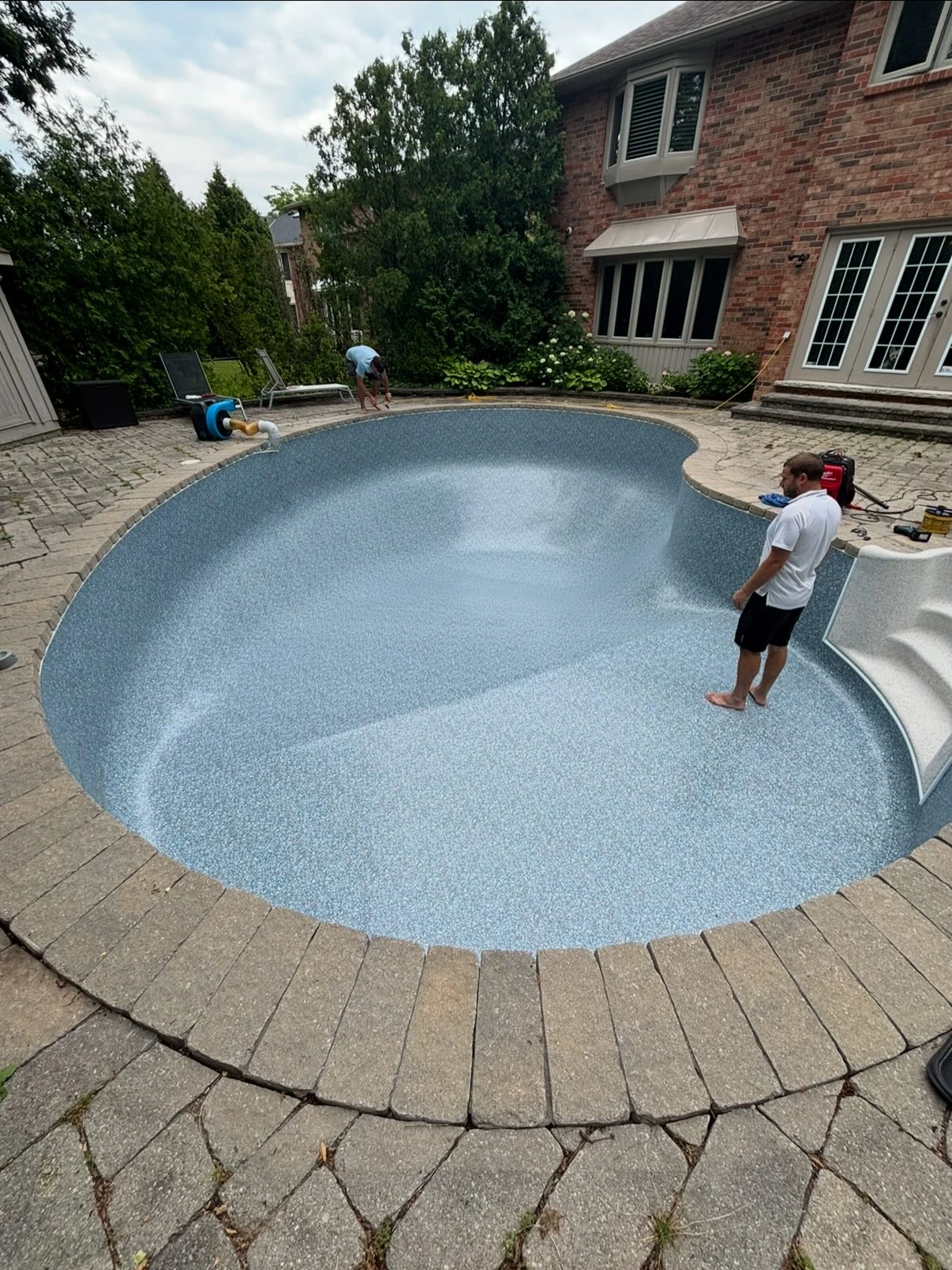 Two Blue Pools technicians installing a new grey liner inside a kidney-shaped pool